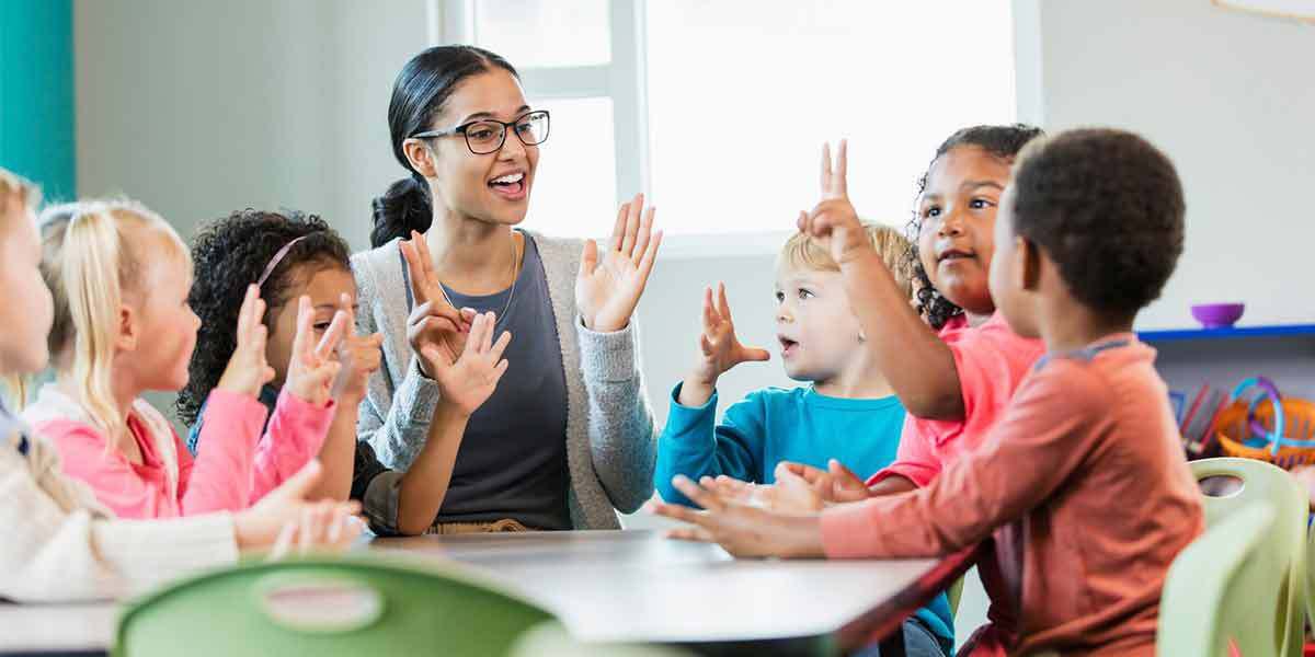 Teacher surrounded by children playing games1200x600